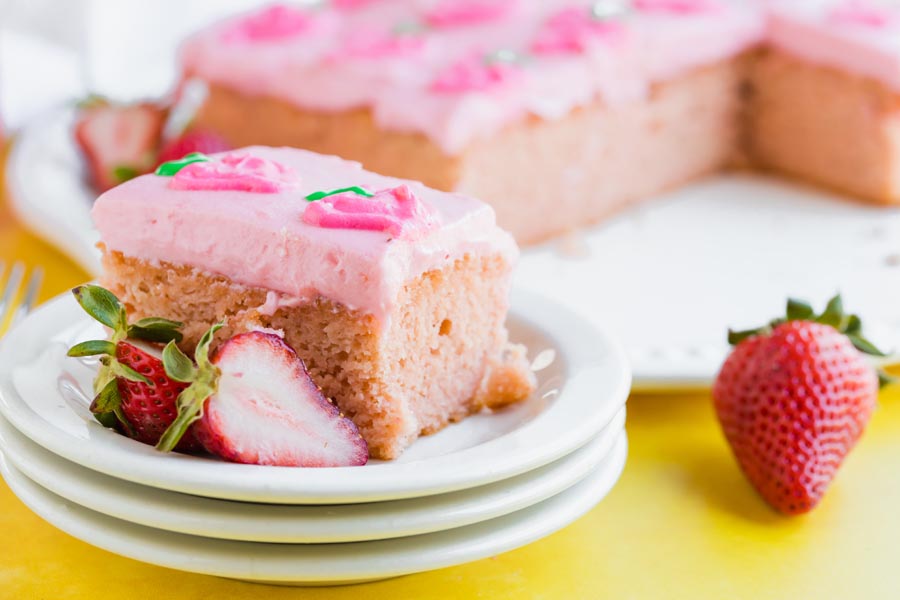 slice of strawberry cake on a stack of white plates with strawberries around
