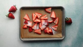 sliced strawberries on a parchment lined baking tray dusted with sugar