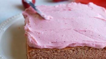 spreading pink strawberry frosting on with a cake spatula