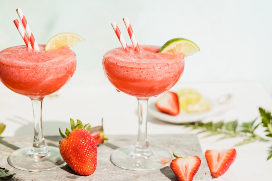 two daiquiri cocktails with strawberries and limes around