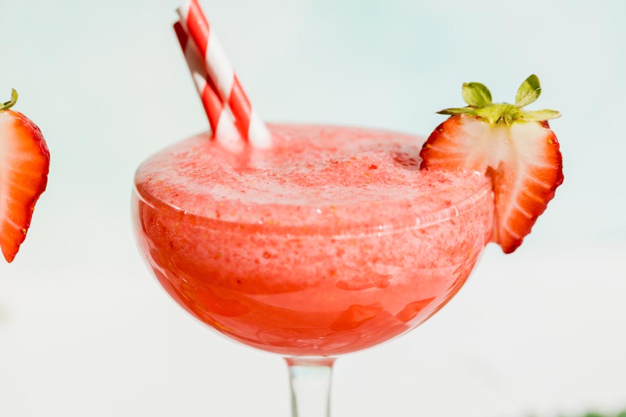 frozen strawberry daiquiri in a wine glass with strawberries on the lip
