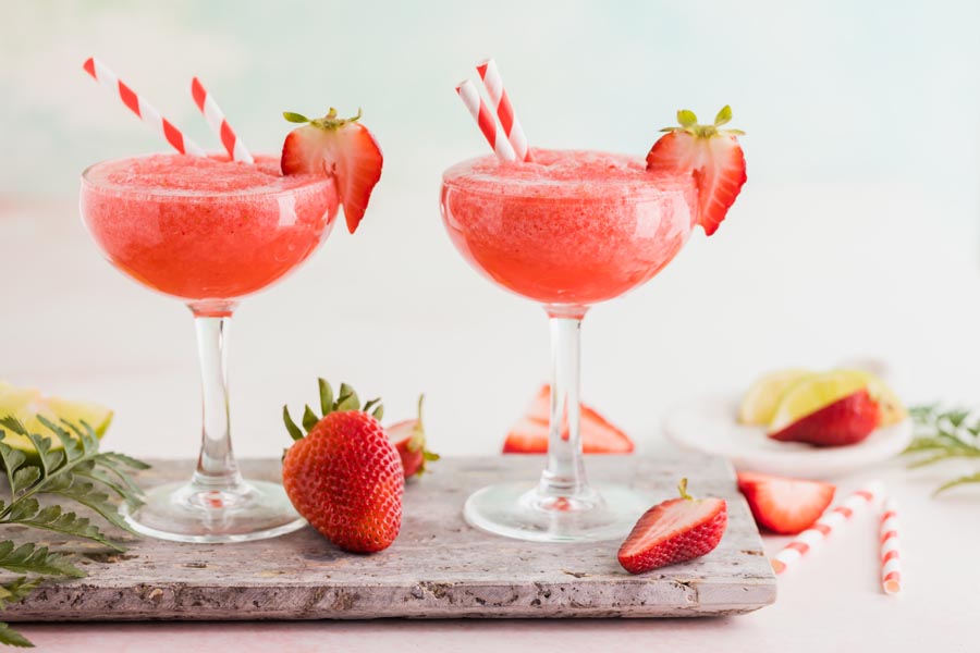 two red refreshing daiquiris with strawberries around