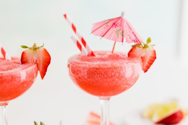 two strawberry daiquiri glasses with an umbrella in it