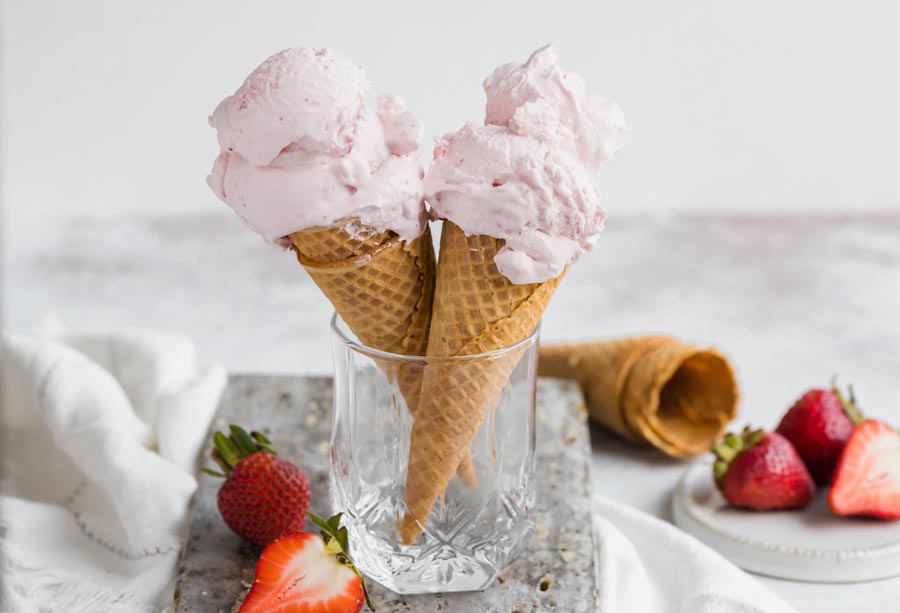 a glass holding strawberry ice cream cones with empty cones and strawberries near