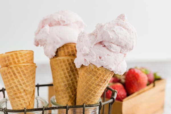 two strawberry ice cream cones with strawberries in the background