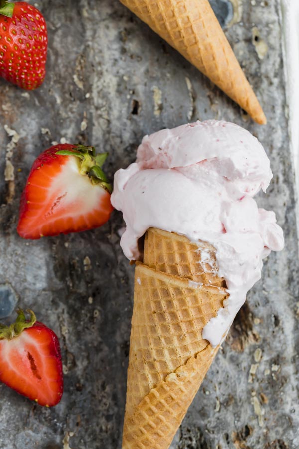 melting strawberry ice cream in a cone next to sliced strawberries