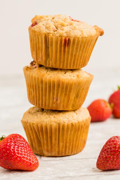 Three muffins stacked on each other with two strawberries in front.