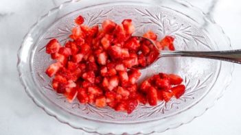 cut strawberries in a glass bowl with a spoon