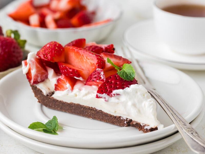 Slice of keto strawberry cream pie with a chocolate crust and fresh strawberries.
