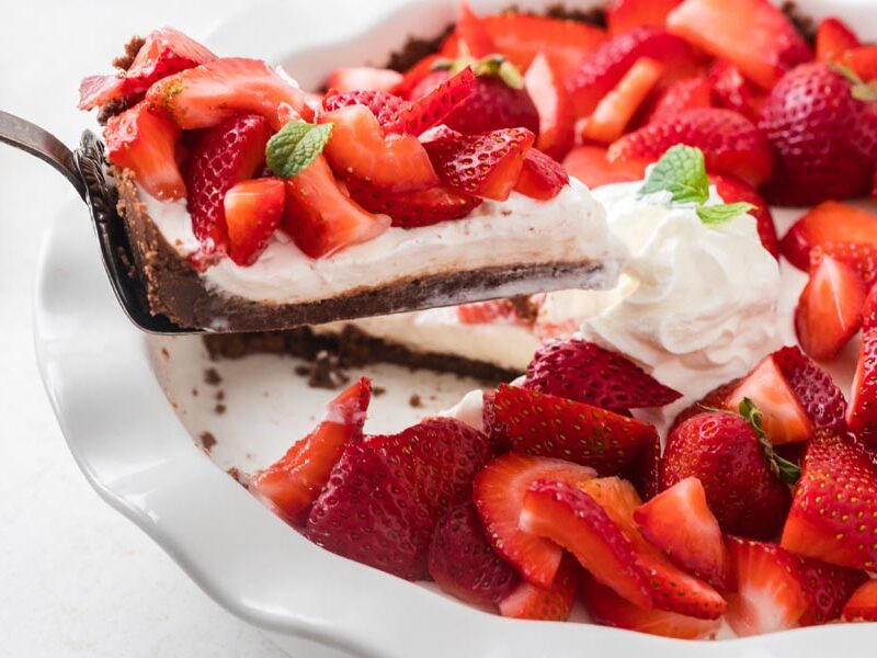 Slice of strawberry pie lifted from a glass dish with whipped cream and fresh berries.