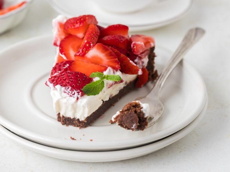 A partially eaten slice of keto strawberry pie on a plate with a fork holding a bite of the chocolate crust.