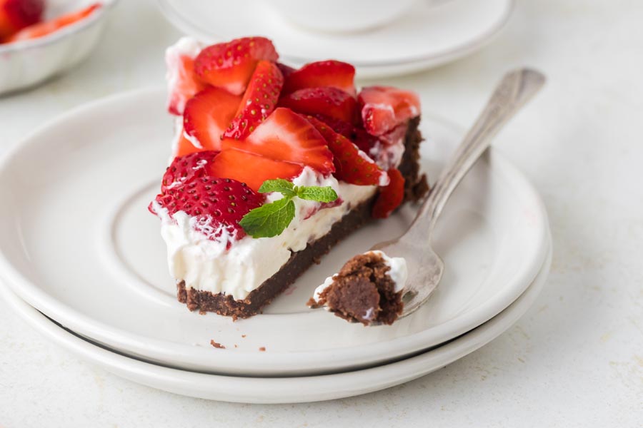 A partially eaten slice of keto strawberry pie on a plate with a fork holding a bite of the chocolate crust.