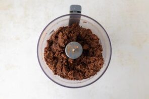 A food processor bowl filled with blended chocolate crust mixture.
