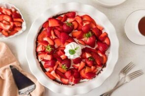 Finished strawberry pie with whipped topping in the center, surrounded by sliced and whole strawberries.