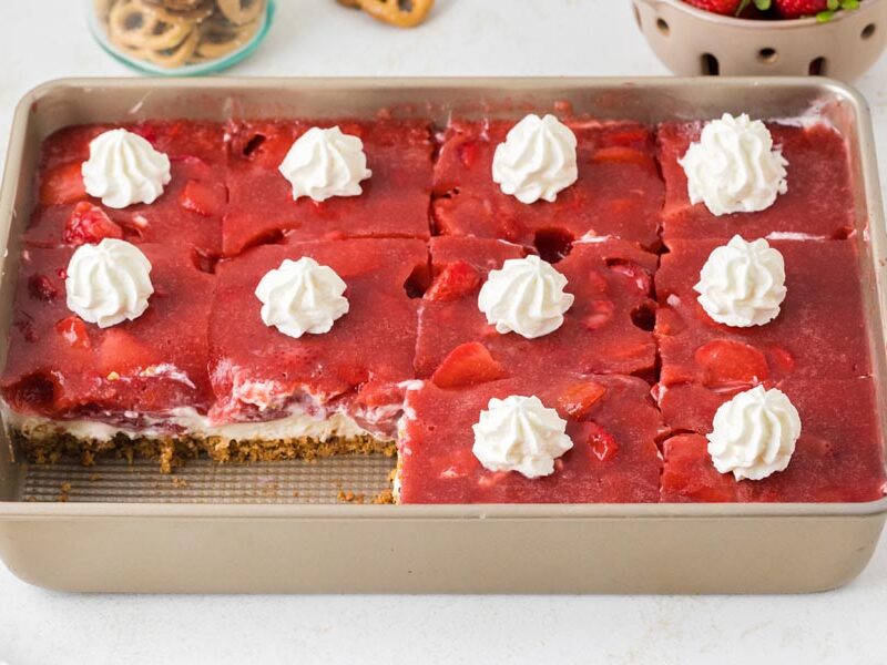 Pan of strawberry pretzel salad topped with whipped cream, with one piece removed.