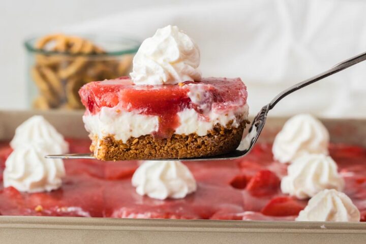 A slice of keto strawberry pretzel salad with layers of pretzel crust, cream cheese filling, and strawberry gelatin held on a spatula.