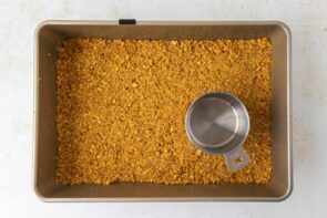 Crust mixture packed into a baking dish using a measuring cup.