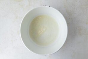 A white bowl holding bloomed gelatin before it’s added to the strawberry layer.
