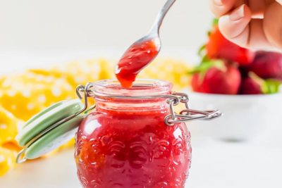 a spoon dripping strawberry sauce over a jar