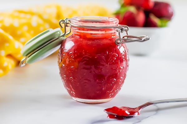 strawberry sauce in a jar with a spoon holding sauce in front