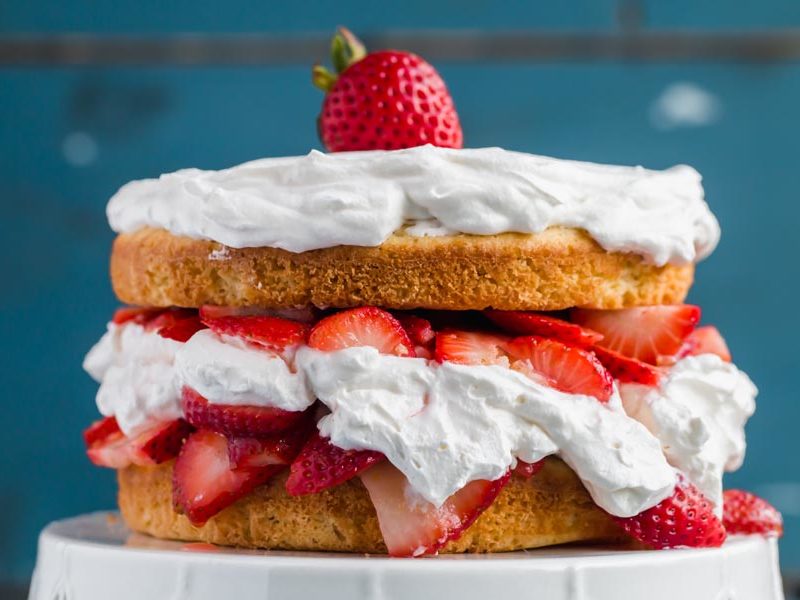 Keto strawberry shortcake layered with whipped cream and strawberries on a white cake stand.