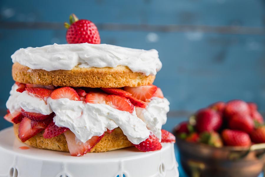 strawberry shortcake sitting in front of a white background with fresh strawberries and whipped cream squeezing out