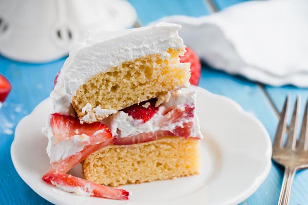 two layers of keto biscuit shortcake with fresh sliced strawberries and whipped cream assembled on top on a white plate