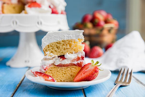 sliced of low carb strawberry shortcake on a small plate with a whole cake on a cake stand in the background