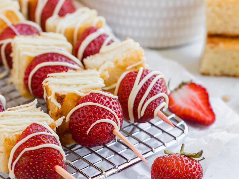 alternating strawberries and cake on skewers on a wire rack