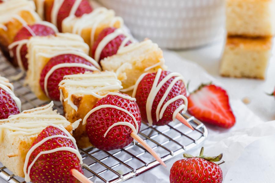 alternating strawberries and cake on skewers on a wire rack