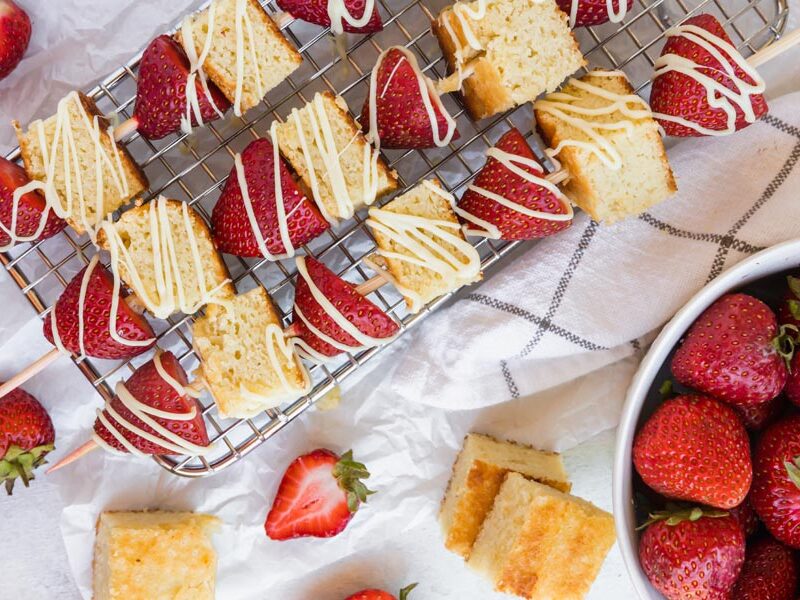 strawberry shortcake kebabs on a wire rack next to a bowl of strawberries
