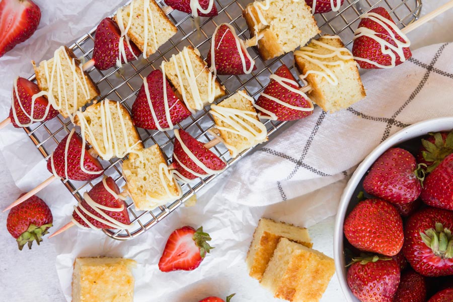 strawberry shortcake kebabs on a wire rack next to a bowl of strawberries