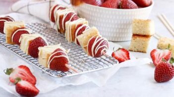 two kebabs on a rack with cake and strawberries near by