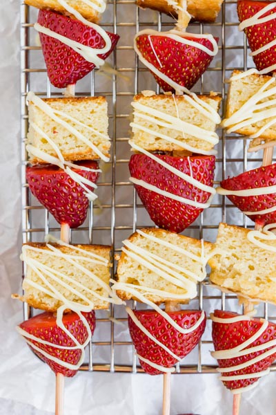 three dessert kebabs on a rack with cake and red strawberries