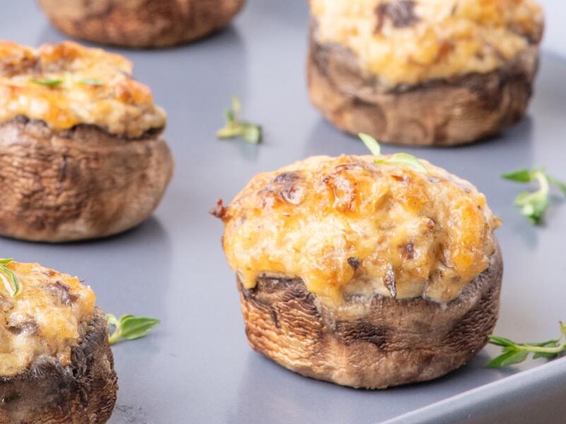 Cheesy stuffed mushrooms on a tray next to fresh thyme.