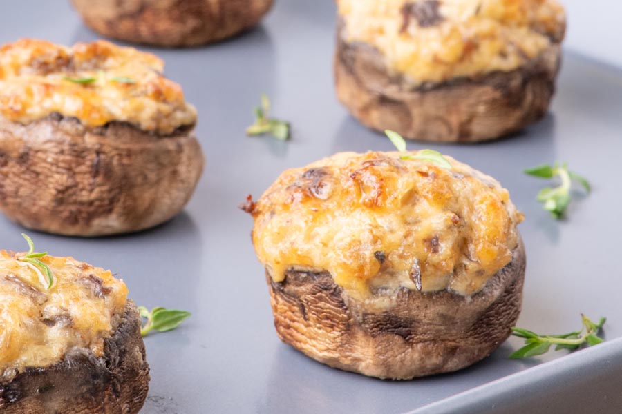 Cheesy stuffed mushrooms on a tray next to fresh thyme.