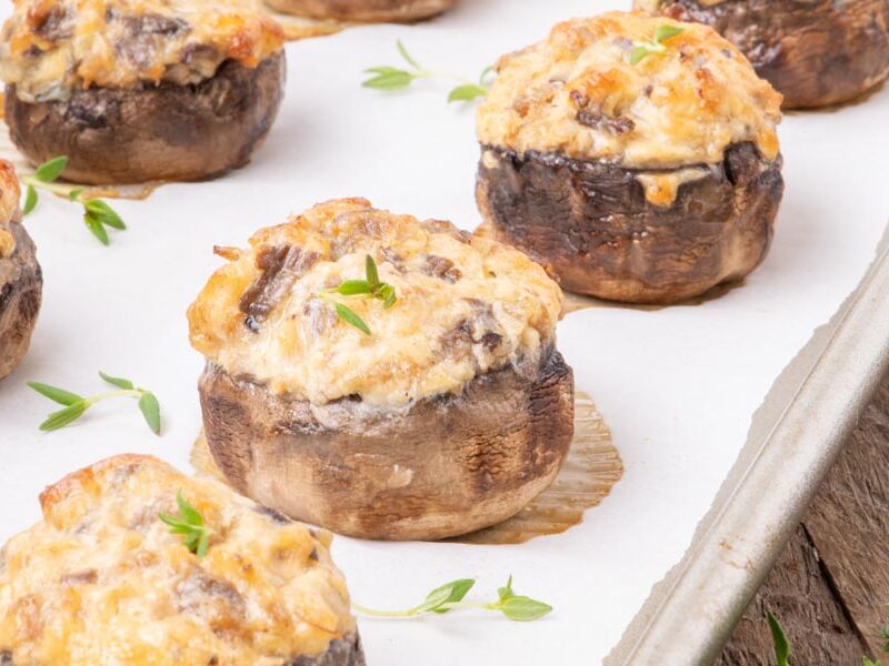 Large stuffed mushrooms stuffed with a mound of cheesy sausage mixture on a parchment lined tray and topped with thyme leaves.