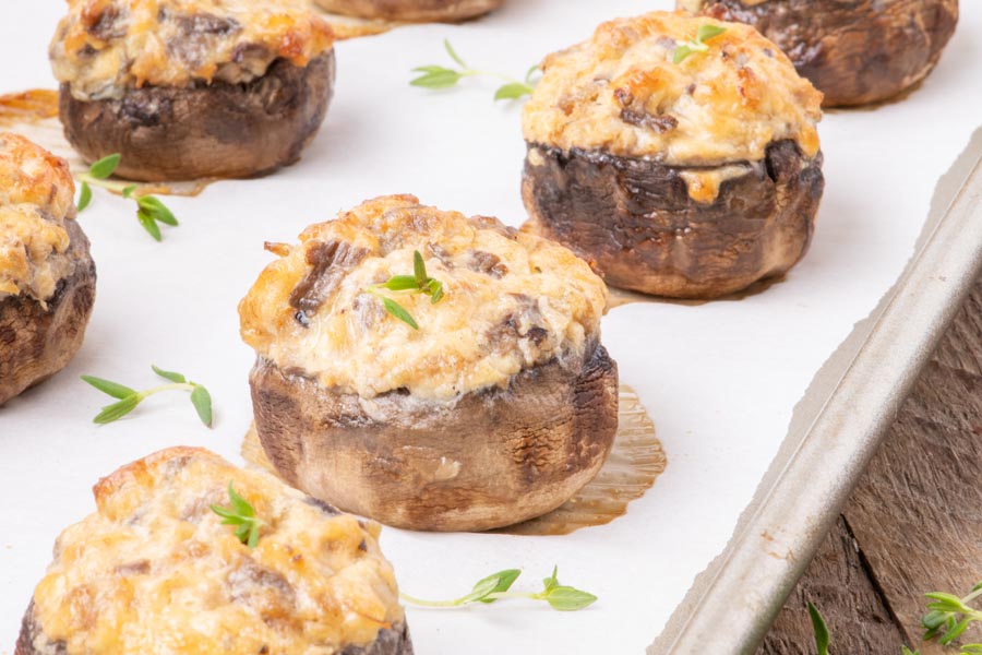 Large stuffed mushrooms stuffed with a mound of cheesy sausage mixture on a parchment lined tray and topped with thyme leaves.