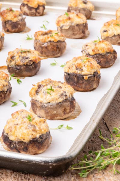 Sausage and cheese filled stuffed mushrooms on a baking tray next to fresh thyme.