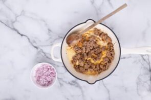 A skillet with cooked sausage next to a bowl of diced shallot.