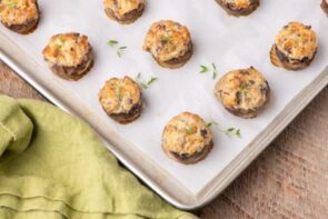 Baked stuffed mushrooms on a parchment lined tray next to a green linen napkin.