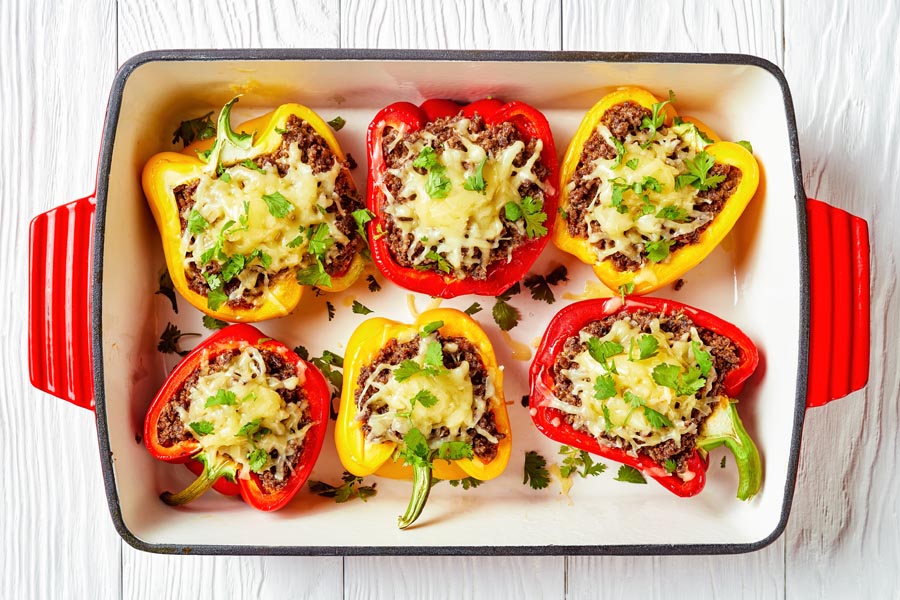 a baking dish with stuffed peppers topped with cheddar cheese and cilantro