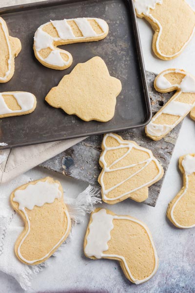 Christmas cookies decorated with white frosting on a baking tray and on the counter.