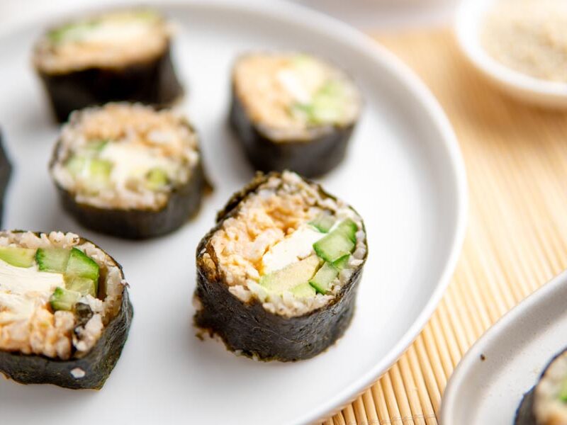 California rolls sitting on a white plate over a bamboo mat.