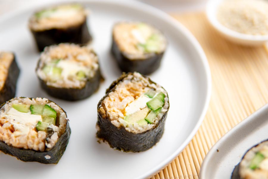 California rolls sitting on a white plate over a bamboo mat.