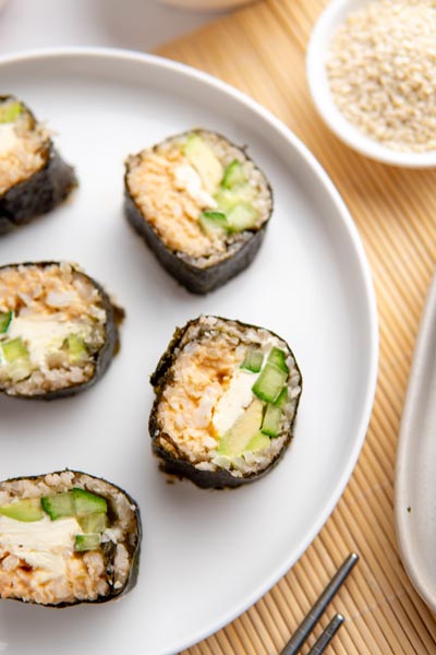 Keto sushi rolls on a plate next to sesame seeds in a bowl.