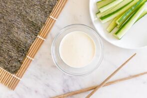 A bowl of creamy wasabi next to sliced cucumber on a plate.