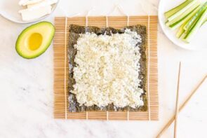 A bamboo mat for sushi with a seaweed sheet on top and cauliflower rice spread over.