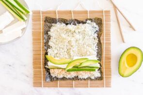 Sushi ingredients line the bottom of a nori sheet topped with cauliflower ready to roll.