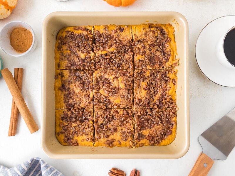 Sliced sweet potato casserole with pecan topping beside cinnamon sticks and coffee.